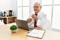 Senior man working at the office using computer laptop in hurry pointing to watch time, impatience, looking at the camera with Royalty Free Stock Photo