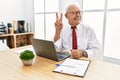Senior man working at the office using computer laptop smiling looking to the camera showing fingers doing victory sign Royalty Free Stock Photo