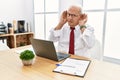 Senior man working at the office using computer laptop trying to hear both hands on ear gesture, curious for gossip Royalty Free Stock Photo