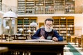 Senior man working in old library, sitting at the table with books and magnifying glass, making notes. Student old man Royalty Free Stock Photo