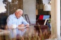 Senior Man Writing Memoirs In Book Sitting At Desk