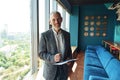 Smiling senior businessman is making notes while standing in modern coworking and looking at camera Royalty Free Stock Photo