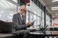 Senior manager text messaging on smart phone while using laptop at the train station lounge Royalty Free Stock Photo