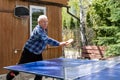 Senior mature grey caucasian old male person making strong ball shot playing ping pong table tennis at home yard garden Royalty Free Stock Photo