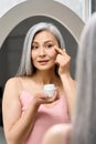 Senior middle aged mature asian woman looking at mirror applying antiage cream.