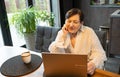 elderly woman in shirt looks at laptop screen smiling at modern kitchen. Royalty Free Stock Photo