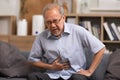 Senior men holding his stomach feeling pain while sitting on the sofa at home. Asian man having stomachache with isolated gastric