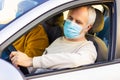 Senior man in a medical face mask driving a car. Coronavirus pandemic concept. Road trip, travel and old people concept - happy se Royalty Free Stock Photo