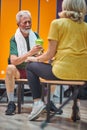 Senior man and woman in gym locker room having a conversation, while sitting on bench facing each other Royalty Free Stock Photo