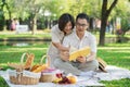 Senior middle aged couple happily embracing and reading a book together during a picnic in the park outdoors. Royalty Free Stock Photo