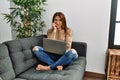 Senior middle east woman using laptop sitting on the sofa at home looking stressed and nervous with hands on mouth biting nails Royalty Free Stock Photo