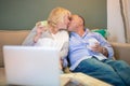 Senior mixed race couple kissing on couch in front of a laptop Royalty Free Stock Photo