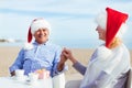 Senior mixed race couple sitting in a beach cafe with coffee cups and Christmas gift, holding hands and smiling Royalty Free Stock Photo