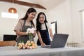 Senior mother and adult daughter happy on the table while arrange flowers in a vase together using laptop computer Royalty Free Stock Photo