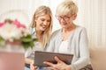 Senior mother and daughter smiling and looking at the tablet. Flower bouquet in foreground.