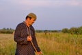 An senior Muslim man in a skullcap and traditional clothes mows hand-scythe grass in a hayfield