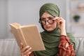 Senior Muslim Woman Having Poor Eyesight Reading Book At Home