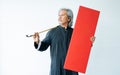 Senior old Asian Chinese man wearing traditional suit, posing, dancing, holding blank red sign to celebrate New Year, standing on