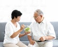 Senior old Asian man and woman lovers eating vegetables salad together on sofa in home Royalty Free Stock Photo