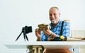 Senior old Caucasian man wearing check shirt, apron, making DIY wooden furniture, using mobile phone, streaming live video clip, Royalty Free Stock Photo