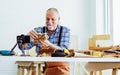 Senior old Caucasian man wearing check shirt, apron, making DIY wooden furniture, using mobile phone, streaming live video clip,