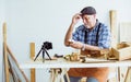 Senior old Caucasian man wearing check shirt, apron, making DIY wooden furniture, using mobile phone, streaming live video clip,