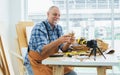 Senior old Caucasian man wearing check shirt, apron, making DIY wooden furniture, using mobile phone, streaming live video clip, Royalty Free Stock Photo