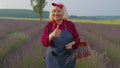 Senior old grandmother farmer gathering lavender flowers on basket on herb garden, showing thumbs up