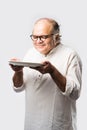 Expressive Indian Old man eating food from empty or blank white plate or bowl