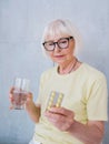 Senior old woman in glasses holding medicine pills and glass of water. Royalty Free Stock Photo