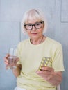 Senior old woman in glasses holding medicine pills and glass of water. Royalty Free Stock Photo