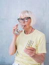 Senior old woman in glasses holding medicine pills and glass of water.