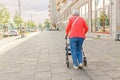 old woman walking alone with walker on the city street, elderly and disability concept