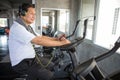 Senior older man  exercising on cycling machine listening music with headphones and phone relaxing in gym. aged . Old male workout Royalty Free Stock Photo