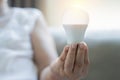 Senior older woman holding a light bulb in her hand while sitting on sofa in the living room at home Royalty Free Stock Photo