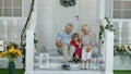 Senior ouple sitting with granddaughter in porch at home. Using mobile phone for online video call