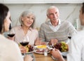 Senior parents sitting at table drinking wine and having conversation with young couple Royalty Free Stock Photo