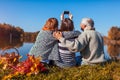 Senior parents taking selfie by autumn lake with their adult daughter. Family values. People having picnic