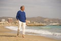 Senior pensioner sitting relaxed on the beach - retired old man on his 70s looking at the sea thoughtful and contemplative with