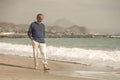 Senior pensioner walking relaxed on the beach - retired old man on his 70s looking at the sea thoughtful and contemplative in