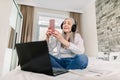 Senior peope and technologies concept. Pretty smiling retired gray haired woman in headphones, sitting on the bed, using