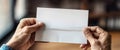 Senior person holds blank folded paper on blurry background closeup. Mature immigrant receives letter from relatives