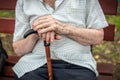 Senior person sitting on wooden bench outdoors. Old man hands holding walking stick. Poverty, loneliness and Royalty Free Stock Photo