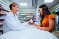 Senior pharmacist selling medication to beautiful young mixed race female over the counter in chemist store