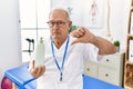 Senior physiotherapy man holding massage body lotion with angry face, negative sign showing dislike with thumbs down, rejection