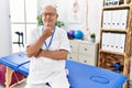 Senior physiotherapy man working at pain recovery clinic looking confident at the camera smiling with crossed arms and hand raised Royalty Free Stock Photo