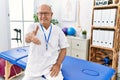 Senior physiotherapy man working at pain recovery clinic smiling friendly offering handshake as greeting and welcoming Royalty Free Stock Photo