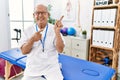 Senior physiotherapy man working at pain recovery clinic smiling and looking at the camera pointing with two hands and fingers to Royalty Free Stock Photo