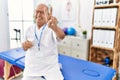 Senior physiotherapy man working at pain recovery clinic smiling looking to the camera showing fingers doing victory sign Royalty Free Stock Photo