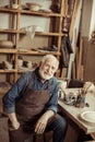 Senior potter in ron sitting at table and looking at camera